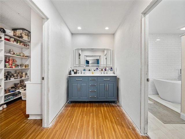 full bathroom featuring double vanity, a sink, a freestanding tub, and wood finished floors