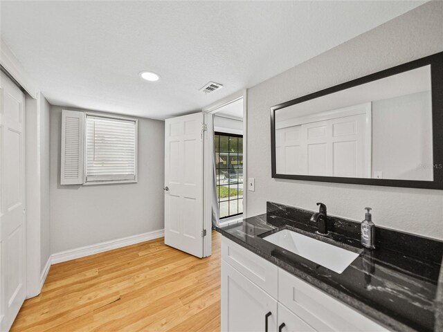 kitchen featuring baseboards, dark stone countertops, light wood-style floors, white cabinets, and a sink