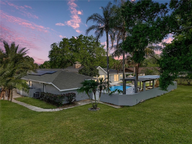 pool at dusk with a yard, an outdoor pool, and central AC