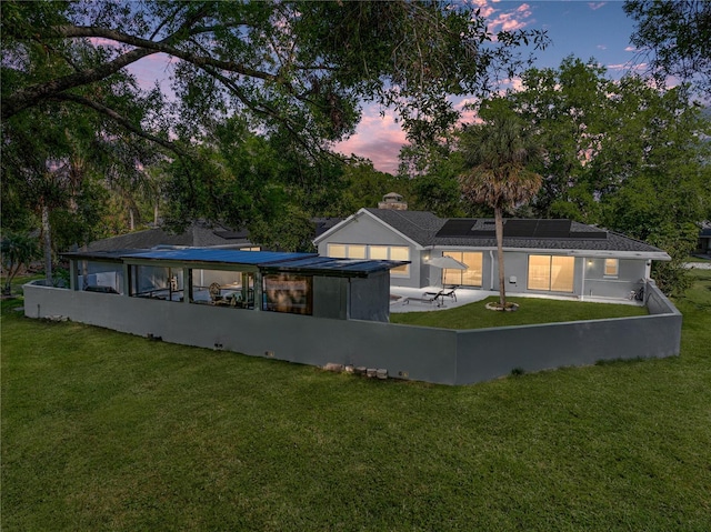 back of house at dusk with roof mounted solar panels, a lawn, and a patio area