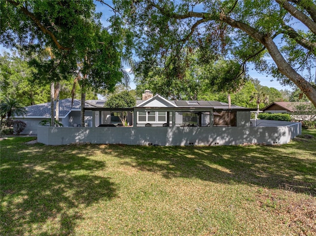 back of property with a lawn, roof mounted solar panels, and a chimney