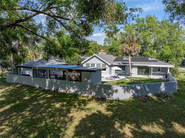 rear view of property with a patio area, roof mounted solar panels, and a yard