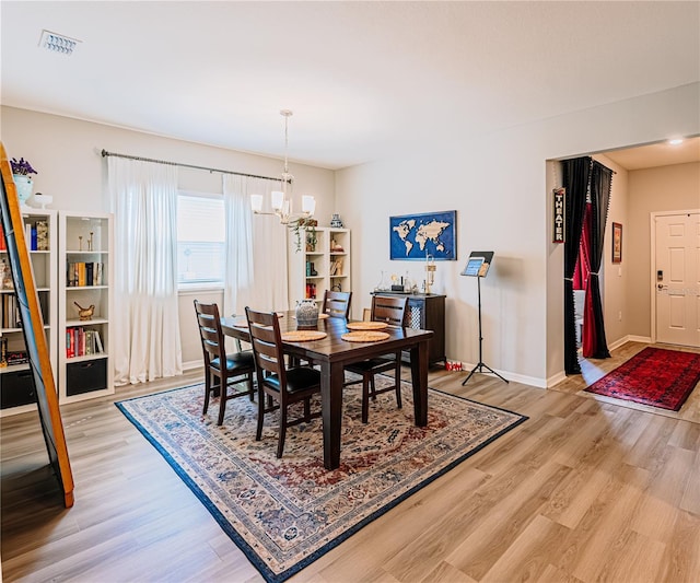 dining space with light wood-style flooring, a notable chandelier, baseboards, and visible vents