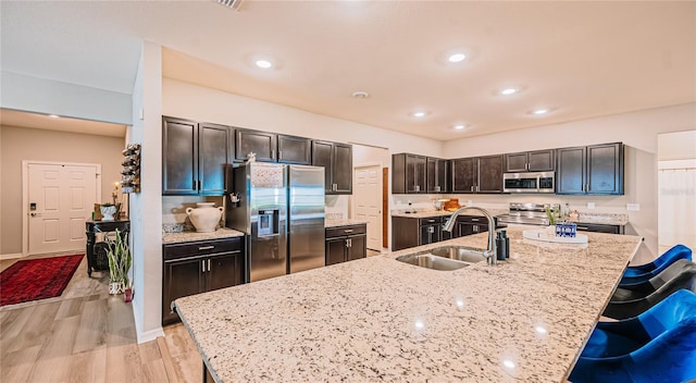 kitchen with light stone counters, a kitchen breakfast bar, light wood-style floors, stainless steel appliances, and a sink