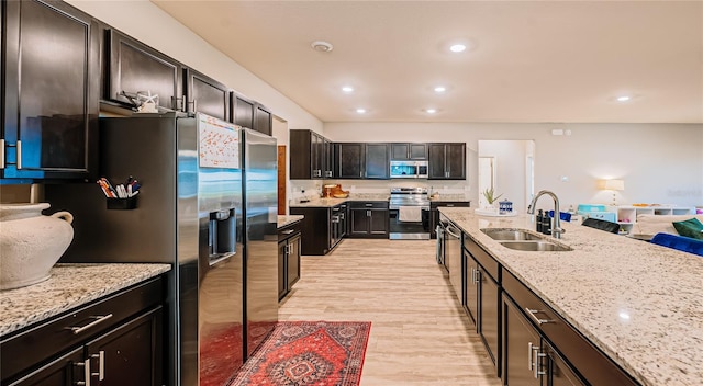 kitchen with a sink, light stone countertops, light wood-style floors, and appliances with stainless steel finishes