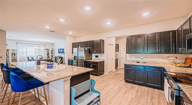 kitchen featuring light wood-type flooring, visible vents, appliances with stainless steel finishes, a breakfast bar area, and light stone countertops