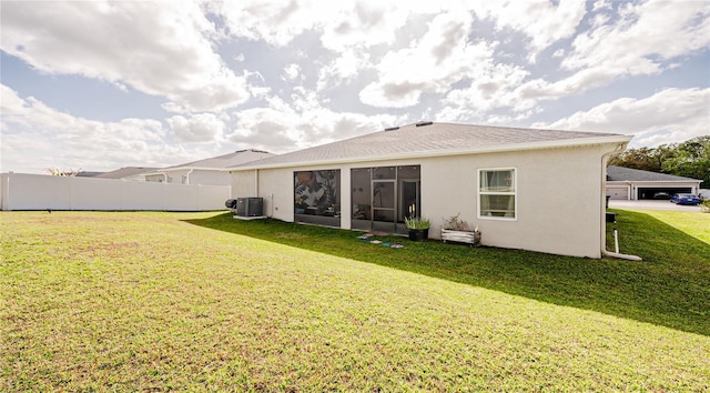 rear view of house featuring stucco siding, a lawn, central AC unit, and fence