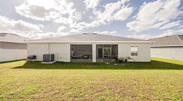 rear view of house featuring fence, a yard, a sunroom, central AC, and stucco siding