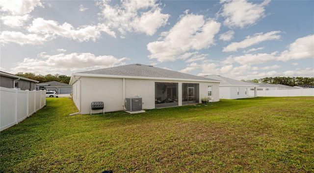 rear view of house with central air condition unit, a yard, fence, and stucco siding