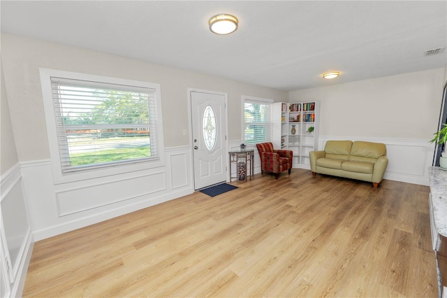 foyer entrance featuring visible vents, wainscoting, and light wood-style floors