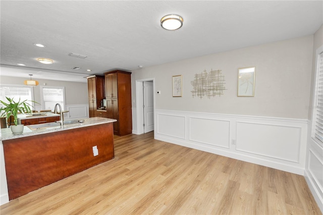 kitchen with light stone counters, visible vents, light wood-type flooring, and a sink