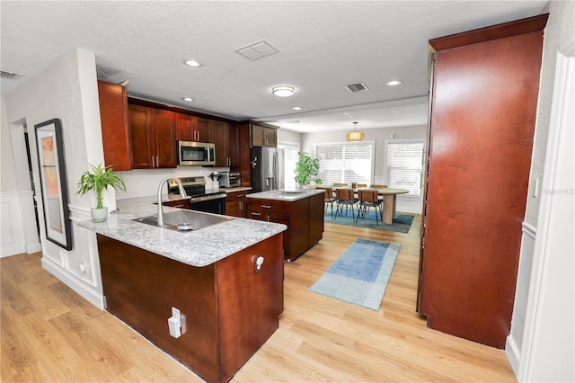 kitchen with visible vents, a kitchen island, a toaster, light wood-style floors, and stainless steel appliances