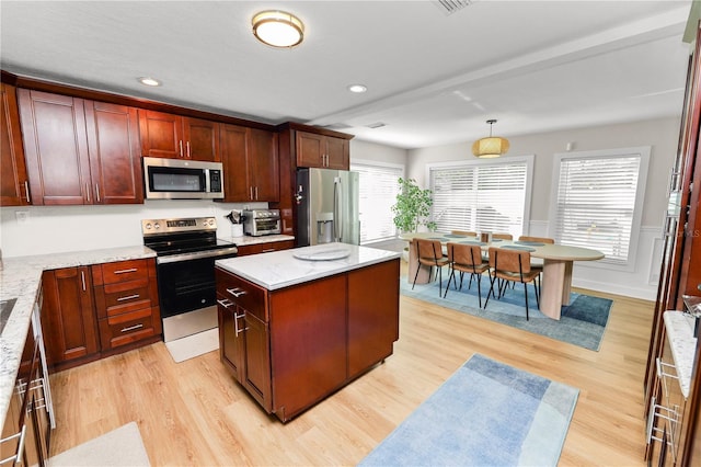 kitchen featuring light wood-type flooring, a kitchen island, appliances with stainless steel finishes, and hanging light fixtures