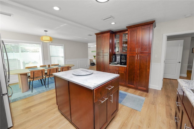 kitchen featuring a kitchen island, light wood-type flooring, freestanding refrigerator, and wainscoting