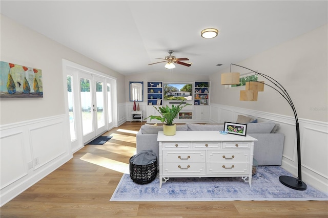 living room featuring french doors, lofted ceiling, wainscoting, and light wood finished floors