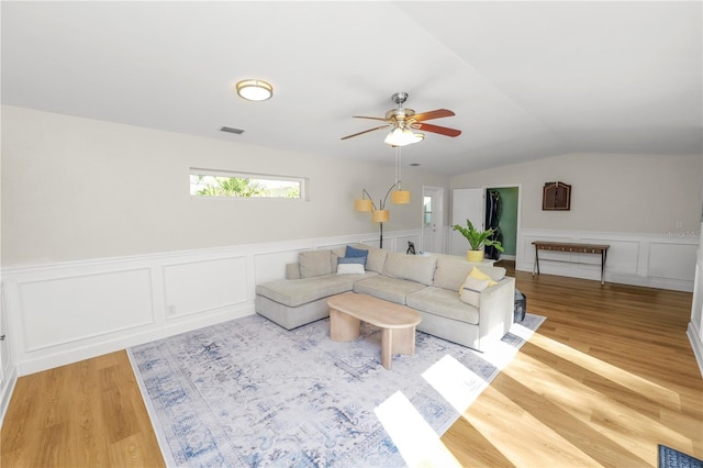 living area featuring visible vents, a ceiling fan, light wood-style floors, wainscoting, and lofted ceiling