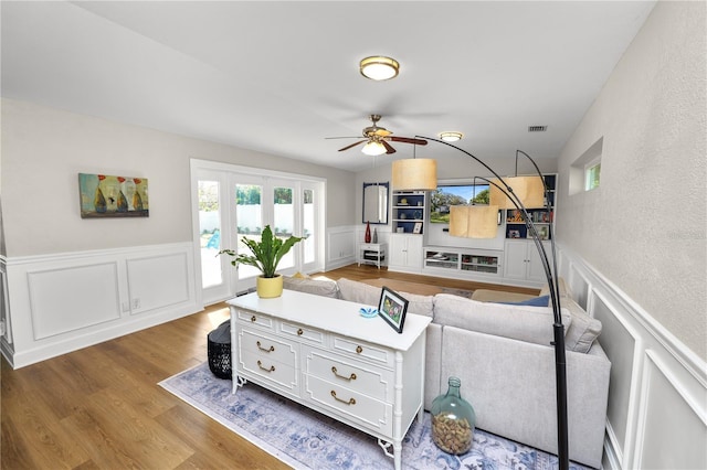 living area with visible vents, a ceiling fan, a wainscoted wall, and wood finished floors