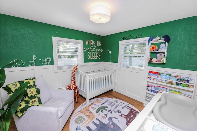 bedroom with wainscoting, a crib, and wood finished floors