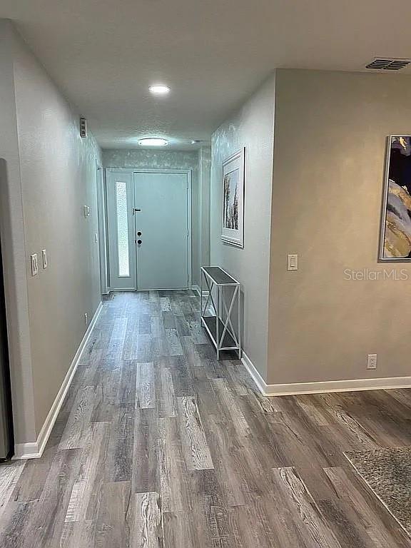 hallway with visible vents, baseboards, and wood finished floors