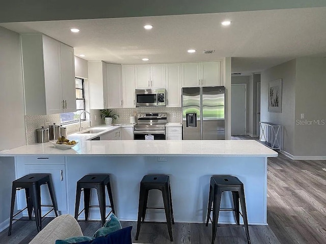 kitchen with light countertops, decorative backsplash, a peninsula, stainless steel appliances, and a sink