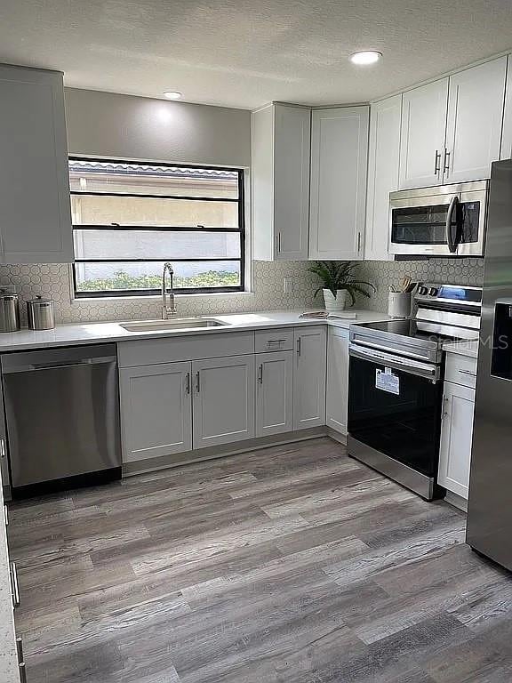 kitchen with a sink, tasteful backsplash, light wood-style floors, and appliances with stainless steel finishes