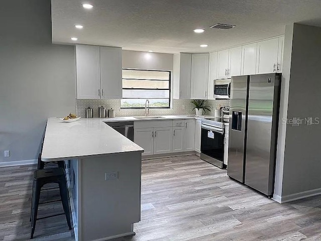 kitchen with visible vents, a peninsula, light wood-style flooring, a sink, and appliances with stainless steel finishes