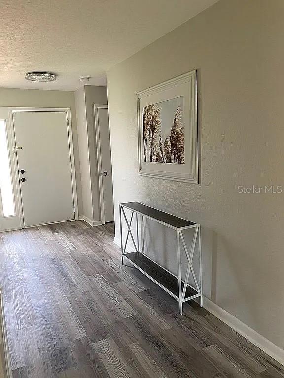 corridor with a textured ceiling, baseboards, and wood finished floors