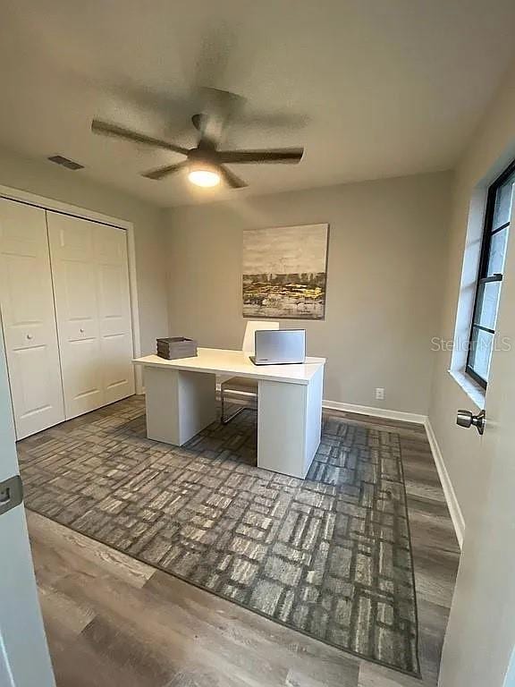 unfurnished office featuring visible vents, baseboards, ceiling fan, and dark wood-style flooring