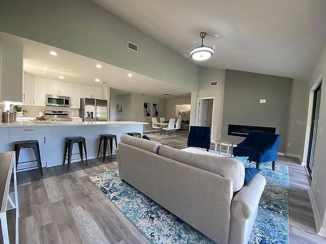 living room with baseboards, visible vents, light wood finished floors, high vaulted ceiling, and recessed lighting