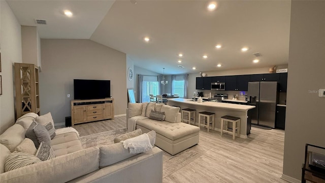 living area with visible vents, baseboards, light wood-style floors, and vaulted ceiling