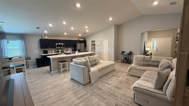 living room featuring lofted ceiling, arched walkways, visible vents, and light wood finished floors