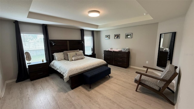 bedroom with a tray ceiling, light wood-style flooring, and baseboards