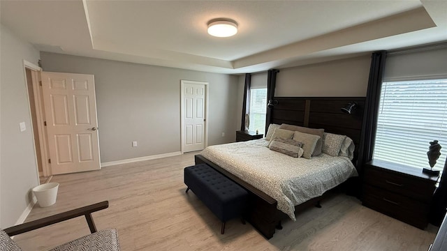 bedroom with a raised ceiling, a closet, baseboards, and light wood finished floors