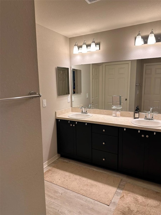 full bathroom featuring double vanity, wood finished floors, baseboards, and a sink