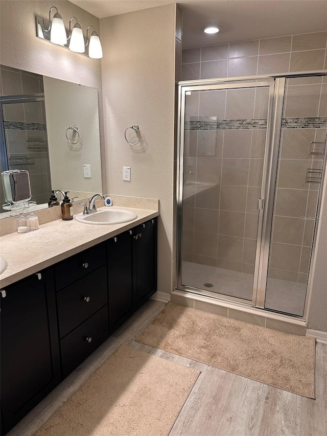 bathroom with a sink, double vanity, wood finished floors, and a shower stall