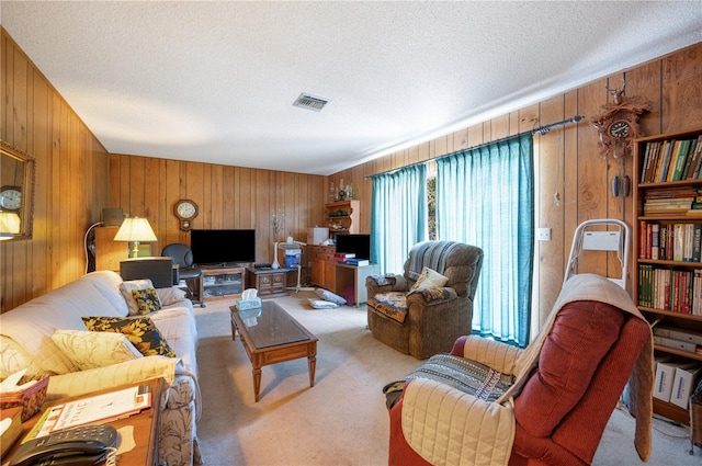 living room with wooden walls, visible vents, carpet floors, and a textured ceiling