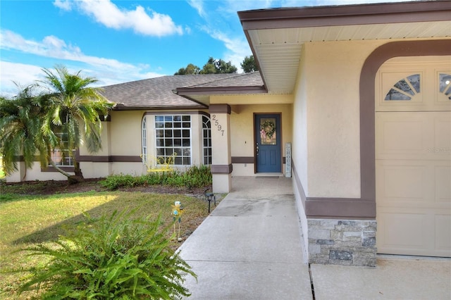 entrance to property featuring stucco siding, a garage, roof with shingles, and a lawn