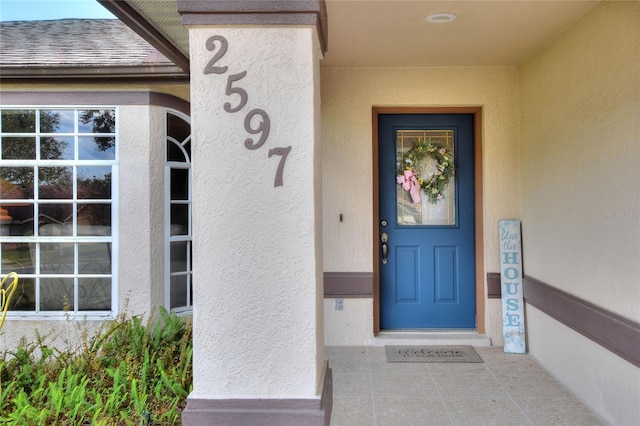 property entrance with roof with shingles and stucco siding