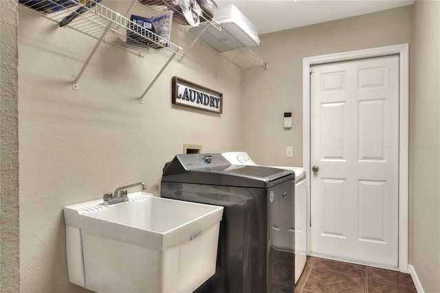 washroom with a sink, dark tile patterned flooring, washing machine and dryer, and laundry area