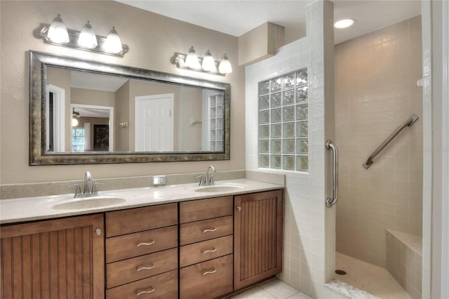 bathroom with double vanity, tile patterned floors, a tile shower, and a sink