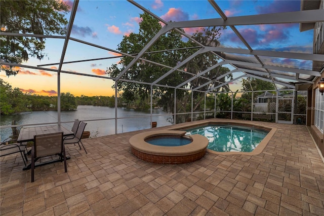 pool at dusk featuring glass enclosure, a patio area, and a pool with connected hot tub