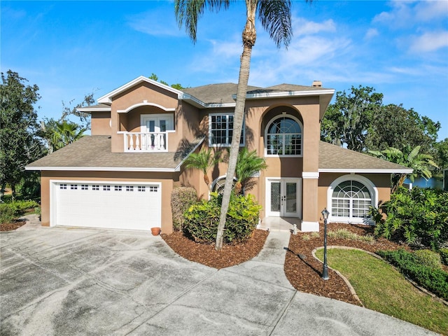 view of front of house with stucco siding, french doors, driveway, and a balcony