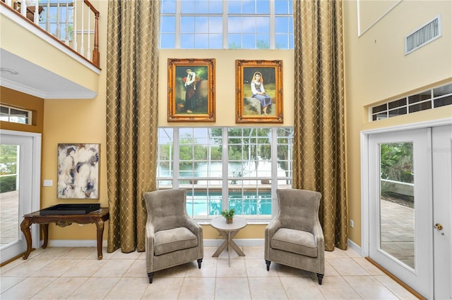 living area featuring visible vents, crown molding, light tile patterned floors, baseboards, and a towering ceiling