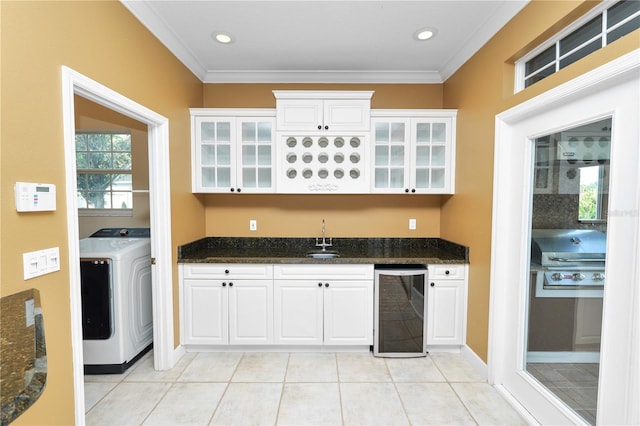 kitchen with beverage cooler, washer / clothes dryer, a sink, white cabinets, and crown molding