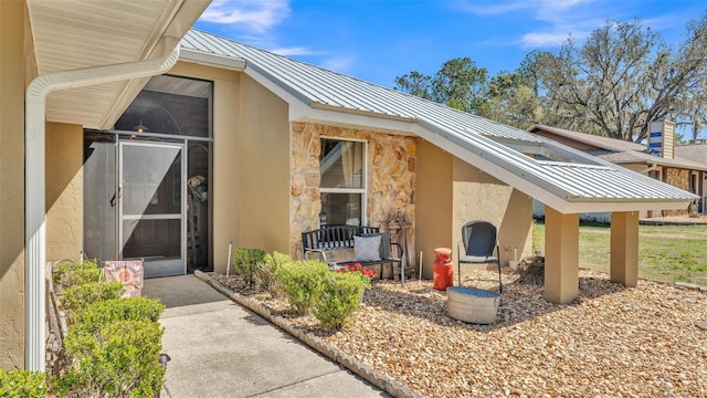 property entrance with stone siding, stucco siding, metal roof, and a standing seam roof