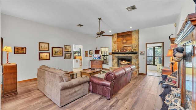 living room with a stone fireplace, light wood-style flooring, a ceiling fan, and visible vents