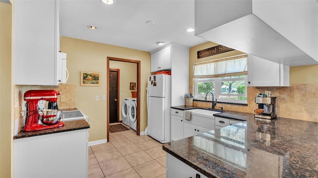 kitchen with light tile patterned floors, freestanding refrigerator, washer and dryer, white cabinetry, and a sink