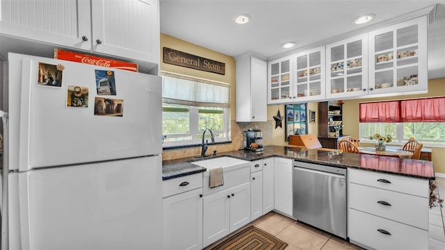 kitchen with light tile patterned floors, freestanding refrigerator, a sink, white cabinets, and dishwasher