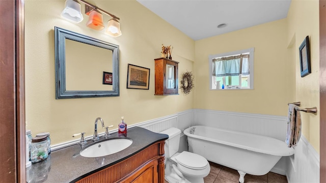 full bath featuring tile patterned flooring, a wainscoted wall, a freestanding bath, toilet, and vanity