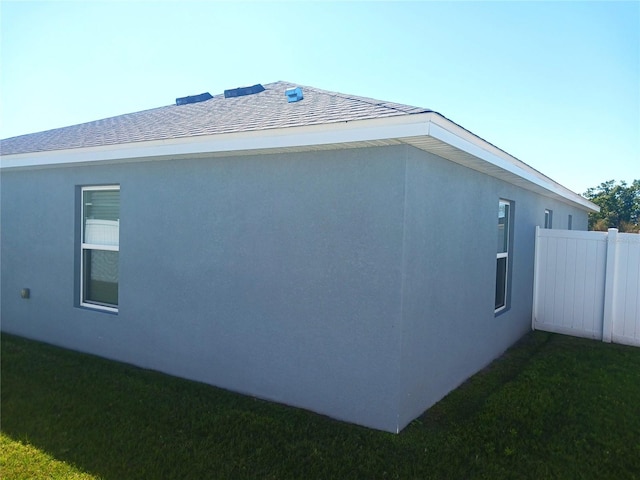 view of home's exterior with stucco siding, a lawn, a shingled roof, and fence